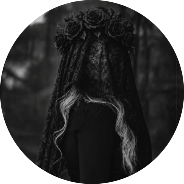 Faceless, seen from the front with the face hidden: a black lace veil crowned with dark roses falls over the head, and long wavy blonde hair shows beneath it. Black and white photograph.