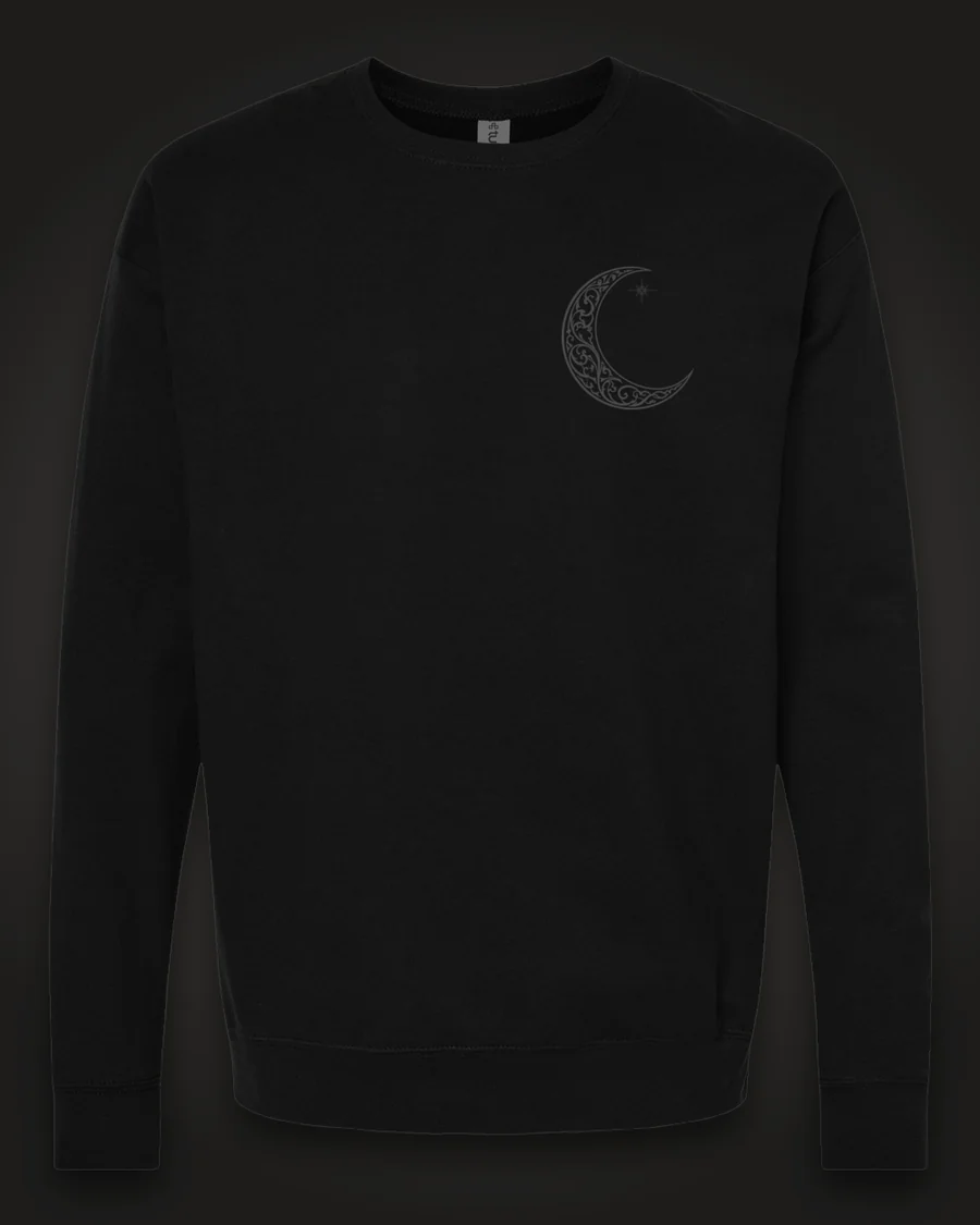 Mockup, front: black crewneck with a small ornate crescent moon on the left chest.