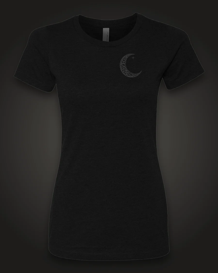 Mockup, front: black women’s tee with a small ornate crescent moon on the left chest.