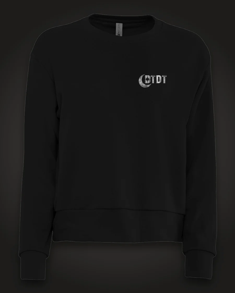 Mockup, front: black women’s crewneck with the DTDT crescent mark in brushed silver on the left chest.