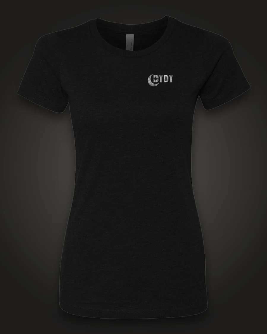 Mockup, front: black women’s tee with the DTDT crescent mark in brushed silver on the left chest.